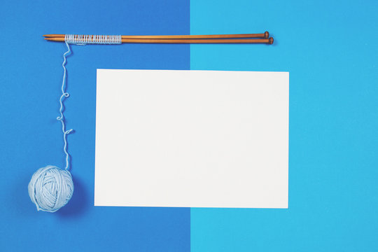 Knitting needles,blue yarn ball and blank sheet of paper on blue background