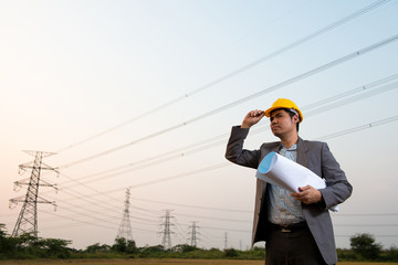 An engineer wear hard yellow hat pose on field worksite to celebration of successful with blueprint in hand