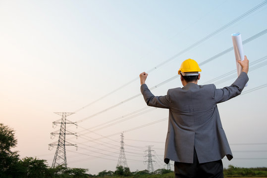An engineer wear hard yellow hat pose on field worksite to celebration of successful with blueprint in hand
