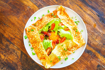 French pancakes crepes with egg and bacon. On a wooden table in the restaurant. The golden pancake crust is neatly wrapped in the filling: egg, bacon, lettuce leaves, tomatoes.Top view with copy space