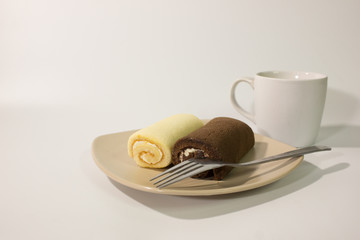 Roll cake with fork and coffee cup on white background.