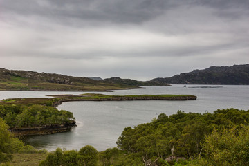 Balgy, Scotland - June 10, 2012: Silver colored Upper Loch Torriden with wide and far view under gray cloudscape. Green hills with trees in front. Mountains on horizon.