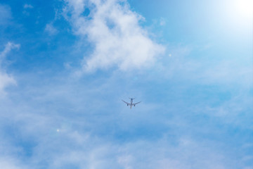 Airplane flying in the blue sky among clouds and sunlight