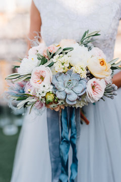 Bride in blue wedding dress holds colorful wedding bouquet with blue and grey ribbon in her arms