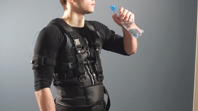 Fit man wearing electro stimulation suit drink water after training.