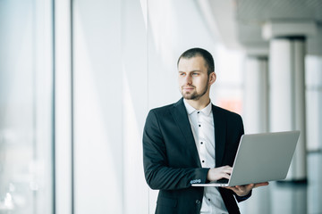 Fototapeta premium Young businessman working on laptop in hands standing in office