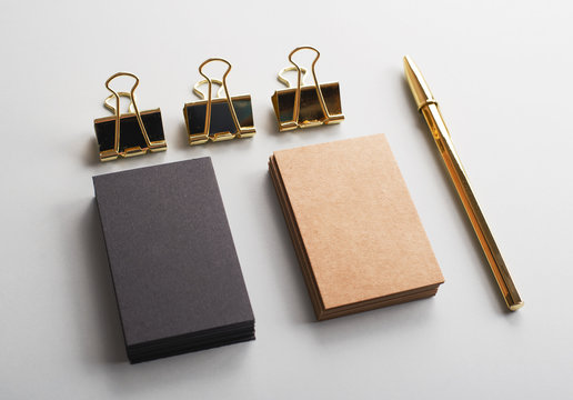 Top view of business cards of brown and black color next to clip and golden ball pen on gray background. Mockup.