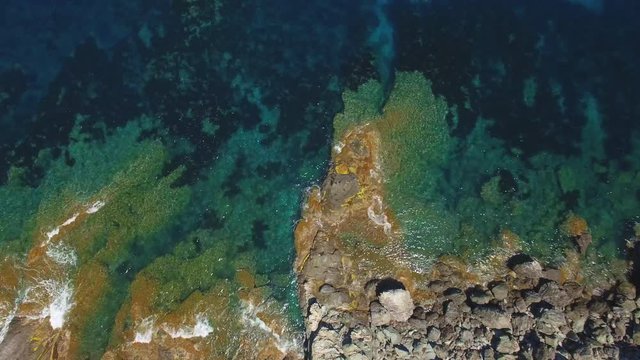 Sea coast aerial shot - beautiful nature. Summer by the ocean - waves breaking on colorful rocks