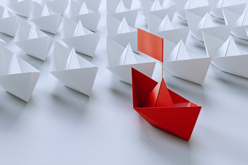 Leadership concept with red paper ship leading among white on white background.