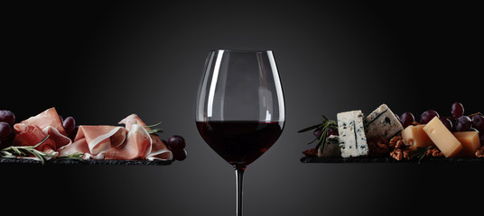 Glas rode wijn met diverse kazen, druiven en prosciutto.