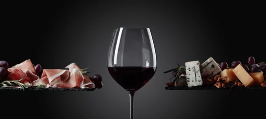 Afwasbaar Fotobehang Wijn Glas rode wijn met diverse kazen, druiven en prosciutto.