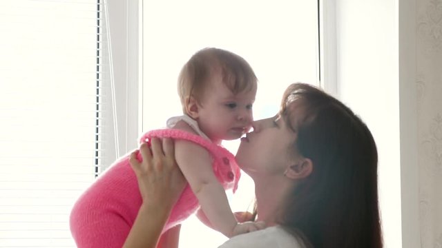 Mom holds baby in arms by window. mom plays with child