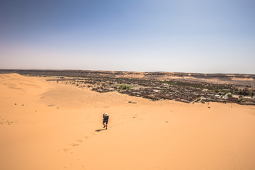 Fototapeta na wymiar Tahgit - June 06, 2017: Western traveler climbing a dune in Taghit, Algeria