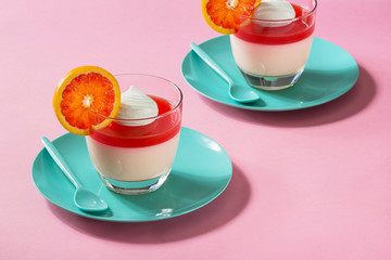 Creamy Citrus Panna Cotta Desserts with Blood Orange Jelly and Whipped Cream on Pink Background