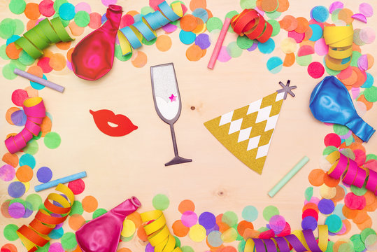 Colorful confetti, streamer and party hat on wooden background from above