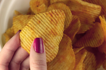 Tasty corrugated chips in female hand. Potato chips, unhealthy food.