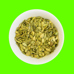 Pumpkin seeds in a bowl isolated on green