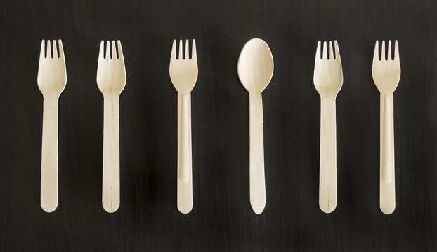 Disposable wooden ecologically designed forks and spoons for takeout meal, food to-go on the black background. Conceptual.