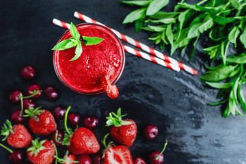 Glass with two straws filled with strawberry smoothie on black with strawberries.