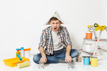 Fun crazy young man in newspaper hat with supermarket grocery push carts for shopping. Instruments for renovation apartment isolated on white background. Wallpaper painting tools. Repair home concept.