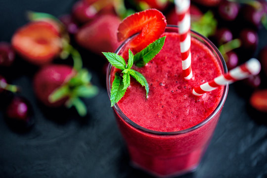 Glass With Two Straws Filled With Strawberry Smoothie On Black With Strawberries.