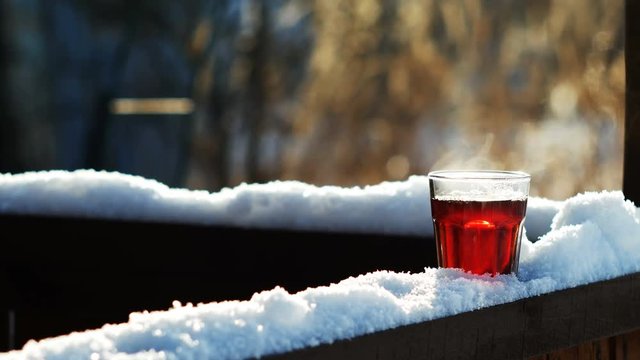 Steaming tea in a glass standing on snow at tree branch, closeup shot