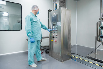 Pharmaceutical factory man worker in protective clothing working with control panel in sterile...
