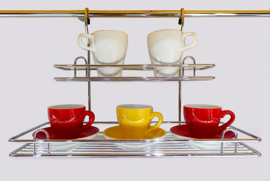 Washed cups on a metal dryer on a white kitchen wall.