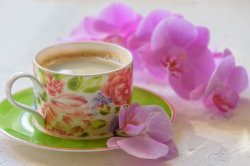 Morning cup of coffee. Sprig of orchid on the table