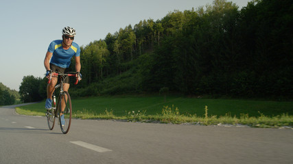 Professional biker goes fast through sunlit spring nature on cool road bicycle.