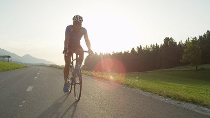 Fototapeta na wymiar SUN FLARE: Young athlete rides his bicycle through picturesque summer nature
