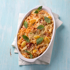 Baked pasta with tomato sauce, garlic, cheese and basil in white ceramic form on a light blue background. Delicious homemade food