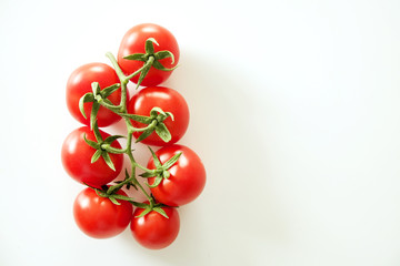 Branch of beautiful juicy organic red cherry tomatoes on white background. Top view of shiny polished glossy vegetables. Clean eating concept. Vegetarian vegan summer detox diet. Copy space, flat lay.