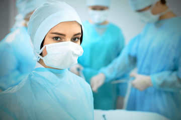 Medical team in masks performing operation. Focus on female doctor or intern girl. Medicine, emergency help concepts