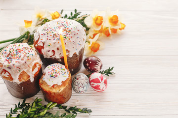 happy Easter concept. stylish painted eggs and easter cake on white rustic wooden background with spring flowers and candle. seasons greetings. space for text. modern easter image