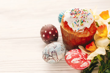 happy Easter concept. stylish painted eggs and easter cake on white rustic wooden background with spring flowers. seasons greetings card. space for text. modern easter image