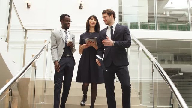 Happy multiracial business people walking down on stairs together with digital tablet.