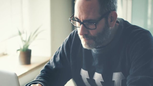 Freelancer with glasses and grey hair working at home on his laptop