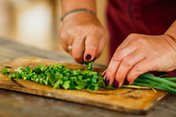 female chef cuts fresh green onion for salad