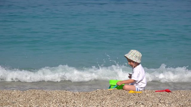 Holiday activity, little child playing with sand at seaside, waves splashing 4K