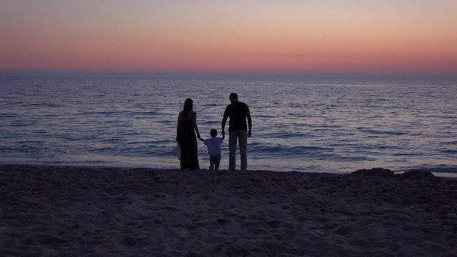 Young family silhouettes having fun on the seashore, twilight 4K
