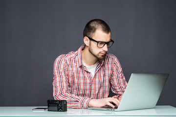 Portrait of young and busy man working on laptop at desk against of grey wall