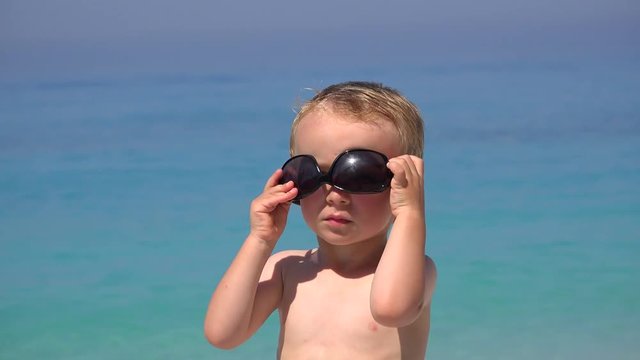 Funny boy try to arrange sunglasses, annoyed to fail, beautiful turquoise sea 4K