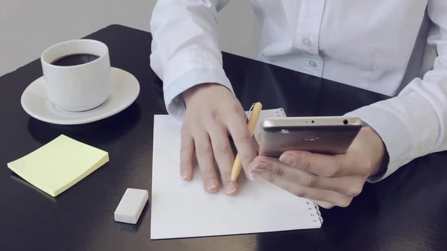 Hands of girl close-up holding a phone Businesswomen at work with mobile phone in office. Scrolls app on your mobile phone. Women works mobile, search on Internet information, makes notes in notepad