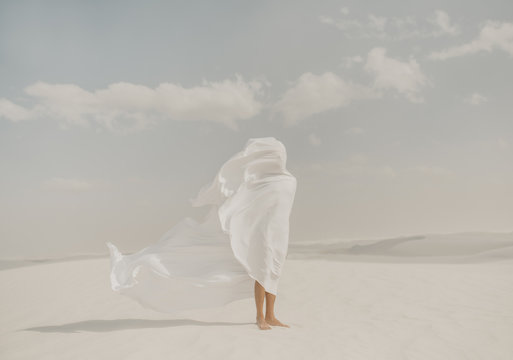 Human standing in desert with a white flow sheet blowing in the wind to the side