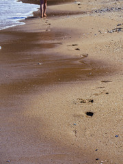 Footprints on the beach and two women legs in the distance