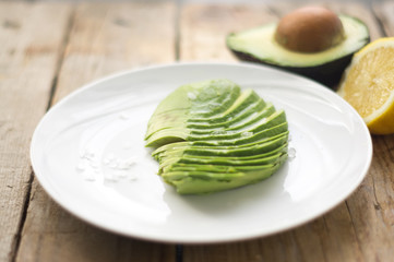 Sliced avocado with salt on the white plate on the wooden rustic table