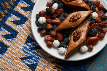 Plate with national pakhlava and snacks for Novruz with glass of tea on wooden table, close-up