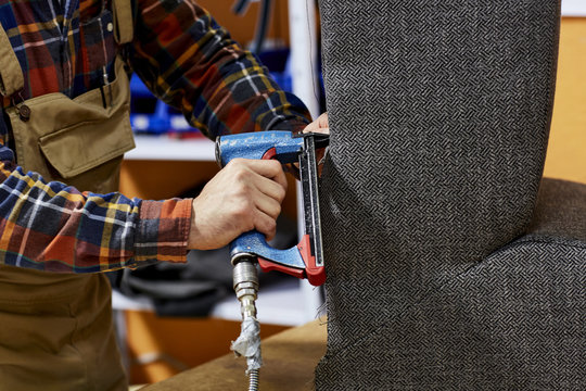 Midsection Of Worker Using Upholstery Gun On Armchair