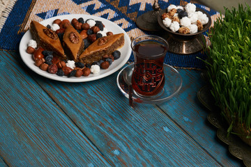 Plate with national pakhlava and snacks for Novruz with glass of tea on wooden table, close-up